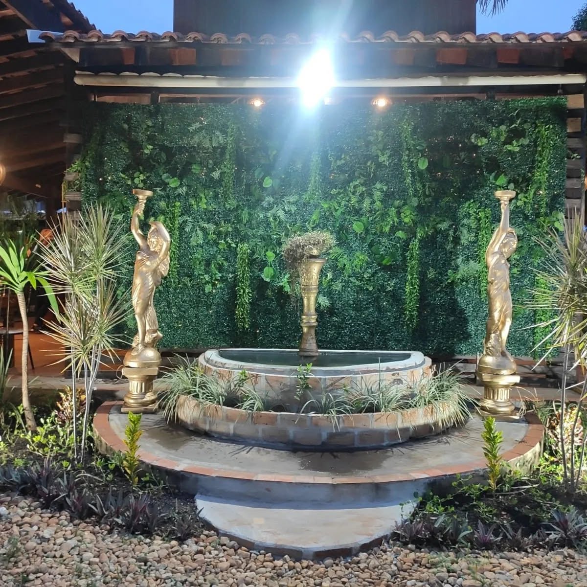 Fonte com painel verde, plantas e esculturas no jardim do espaço