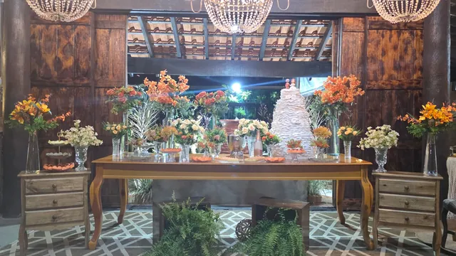 Mesa de bolo com flores alaranjadas, móveis de madeira e lustres suspensos